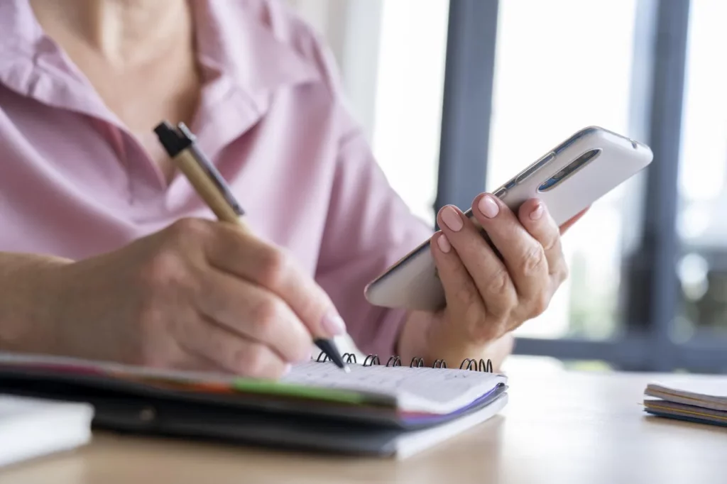 Pessoa segurando celular e escrevendo em agenda